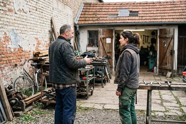 Zwei Handwerker in Arbeitskleidung im Gespräch auf einem Werkstatthof