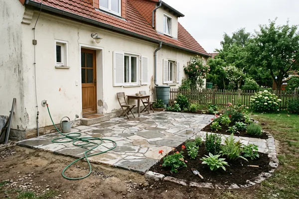 Neu verlegte Natursteinterrasse mit frisch bepflanzten Beeten an einem Wohnhaus